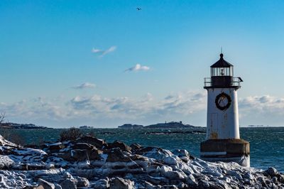 Lighthouse by sea against blue sky