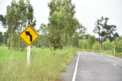 Road sign by trees against sky