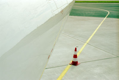 Abstract shot of aircraft fuselage, traffic cone and tarmac.