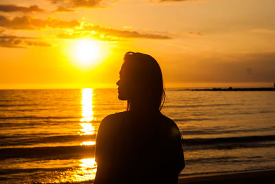 Rear view of silhouette woman standing by sea against sky during sunset