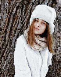 Portrait of woman in snow covered tree trunk during winter