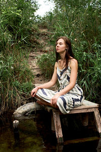 Young woman looking away while sitting on wood against trees