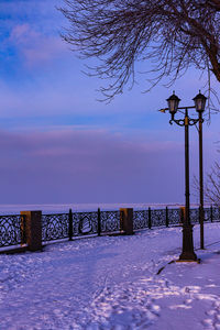 Snow covered street by sea against sky during winter