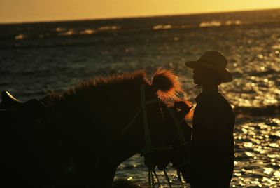 Side view of man with horses standing at beach during sunset