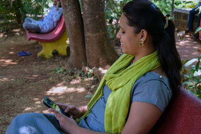 Side view of young woman using mobile phone sitting on bench