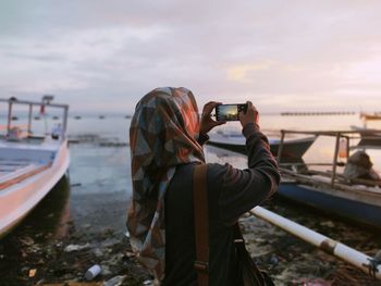 Woman photographing at camera against sky during sunset