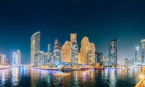 Modern buildings by river against sky at night