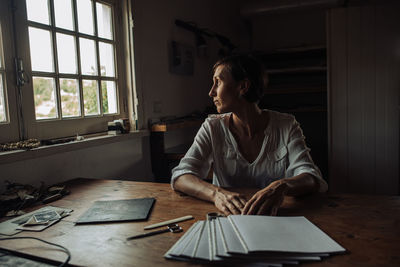 Female artist sitting at table in studio looking at the window