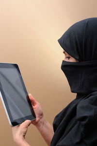 Midsection of man holding camera while standing against wall