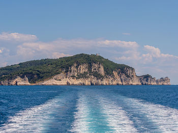 View from a motor boat leaving behind a mountainous island covered by a green forest