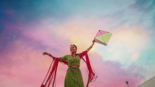 Low angle view of woman holding kite against sky