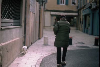 Rear view of woman walking on footpath amidst buildings