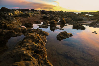 Rocks on shore against sky during sunset