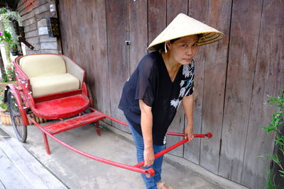 Mature woman wearing asian style conical hat while pulling rickshaw in city