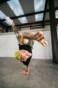 Full body of energetic young man doing acrobatic handstand while performing break dance