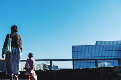 Rear view of mother with daughter walking against clear blue sky