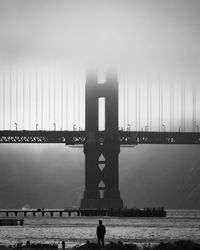 Silhouette man standing by river against bridge