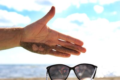 Close-up of hands against sea against sky