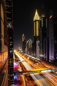 Light trails on road amidst buildings against sky at night