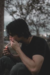 Side view of man smoking cigarette while sitting outdoors