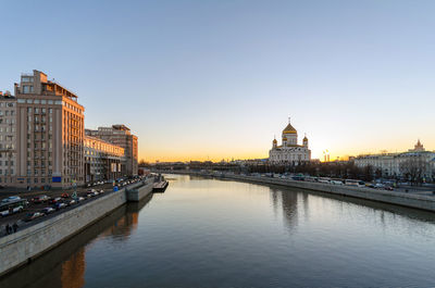 Bridge over river by buildings against sky during sunset