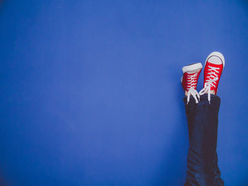 Low section of person wearing canvas shoes by blue wall