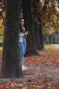 Young woman leaning on tree trunk in forest during autumn