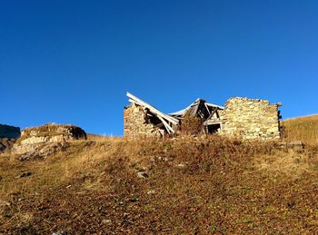 Abandoned house on field against clear blue sky