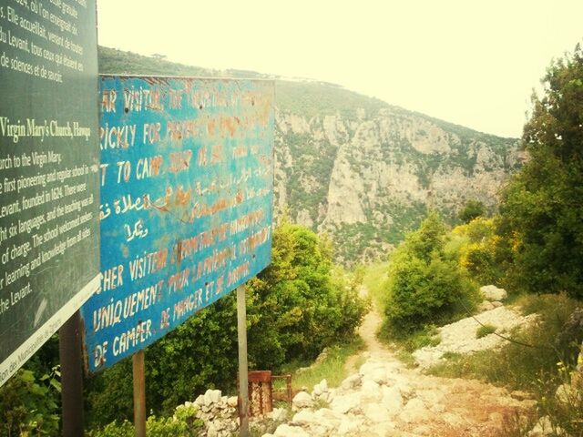 text, western script, mountain, communication, built structure, information sign, architecture, clear sky, sky, graffiti, sign, day, road, plant, tree, non-western script, no people, nature, outdoors, rock formation