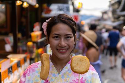 Portrait of smiling young woman holding food while standing on street in city
