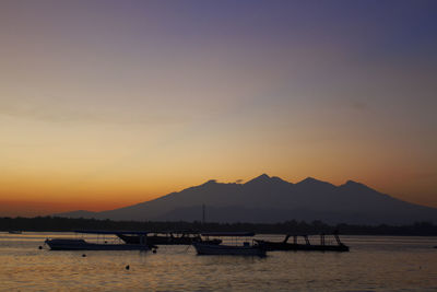 Silhouette boats in sea against orange sky