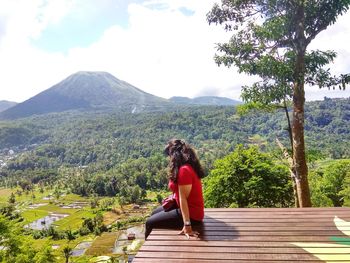 Woman sitting on mountain against sky