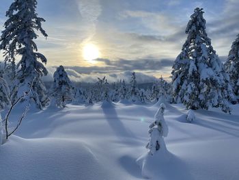 Snow covered field against sky during sunset