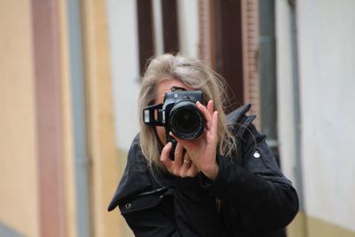 Woman photographing through digital camera against wall