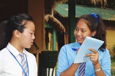 Teenage girl with friend wearing school uniforms writing on note pad