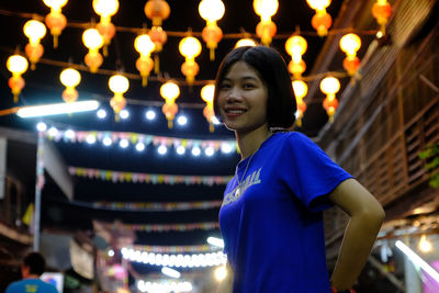 Low angle view of young woman standing against lighting equipments at night