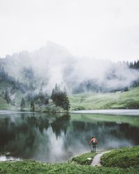 Man holding fishing rod while standing by lake against sky