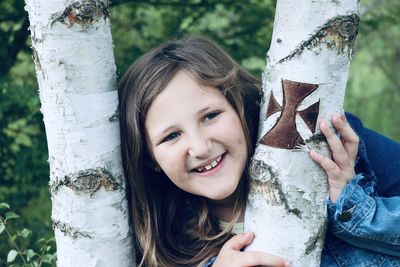 Portrait of a smiling young woman against tree trunk