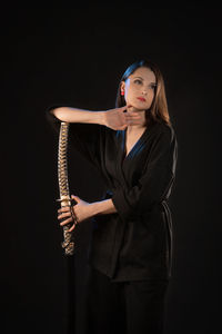 Portrait of young woman standing against black background