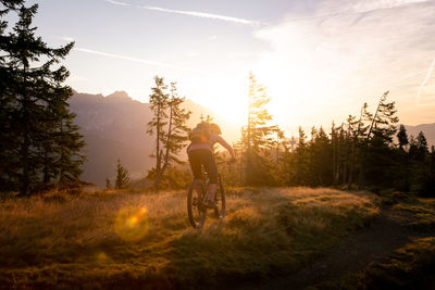 Man riding bicycle on road against sky during sunset