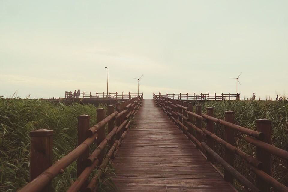 the way forward, tranquility, wood - material, railing, sky, boardwalk, diminishing perspective, tranquil scene, nature, vanishing point, landscape, wooden, scenics, pier, grass, beauty in nature, wood, fence, field, outdoors