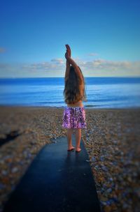 Rear view of girl with arms raised standing on beach against sky