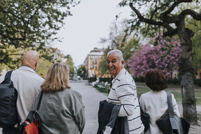 Portrait of smiling senior man looking over shoulder while walking with friends at park