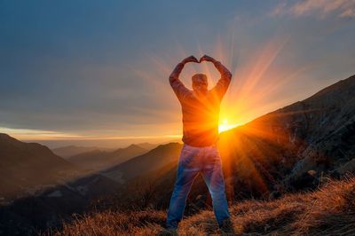 Person standing on mountain against sky during sunset