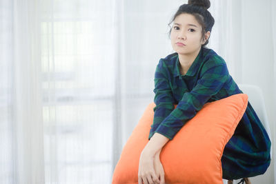 Portrait of young woman sitting at home with pillow