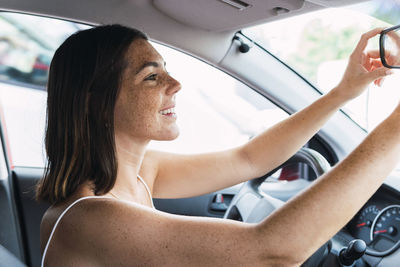 Happy woman arranging rear view mirror in car