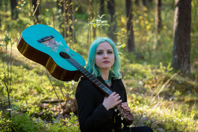 Hipster young woman with turquoise guitar sitting in forest