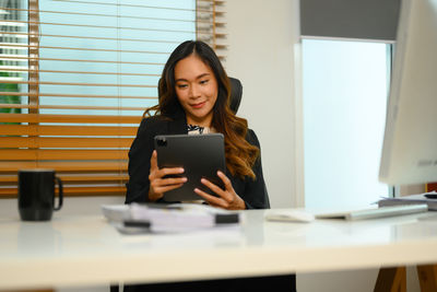 Portrait of young woman using mobile phone at office