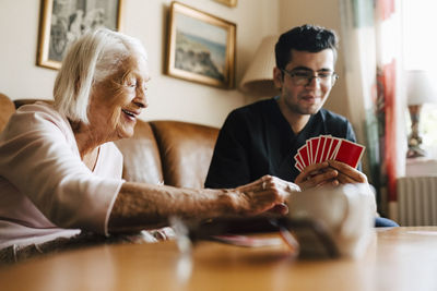 Happy senior woman playing cards with male healthcare worker in living room