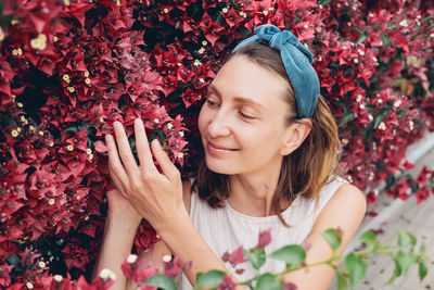 Portrait of tender young woman in dress and headband near bright flowering shrub